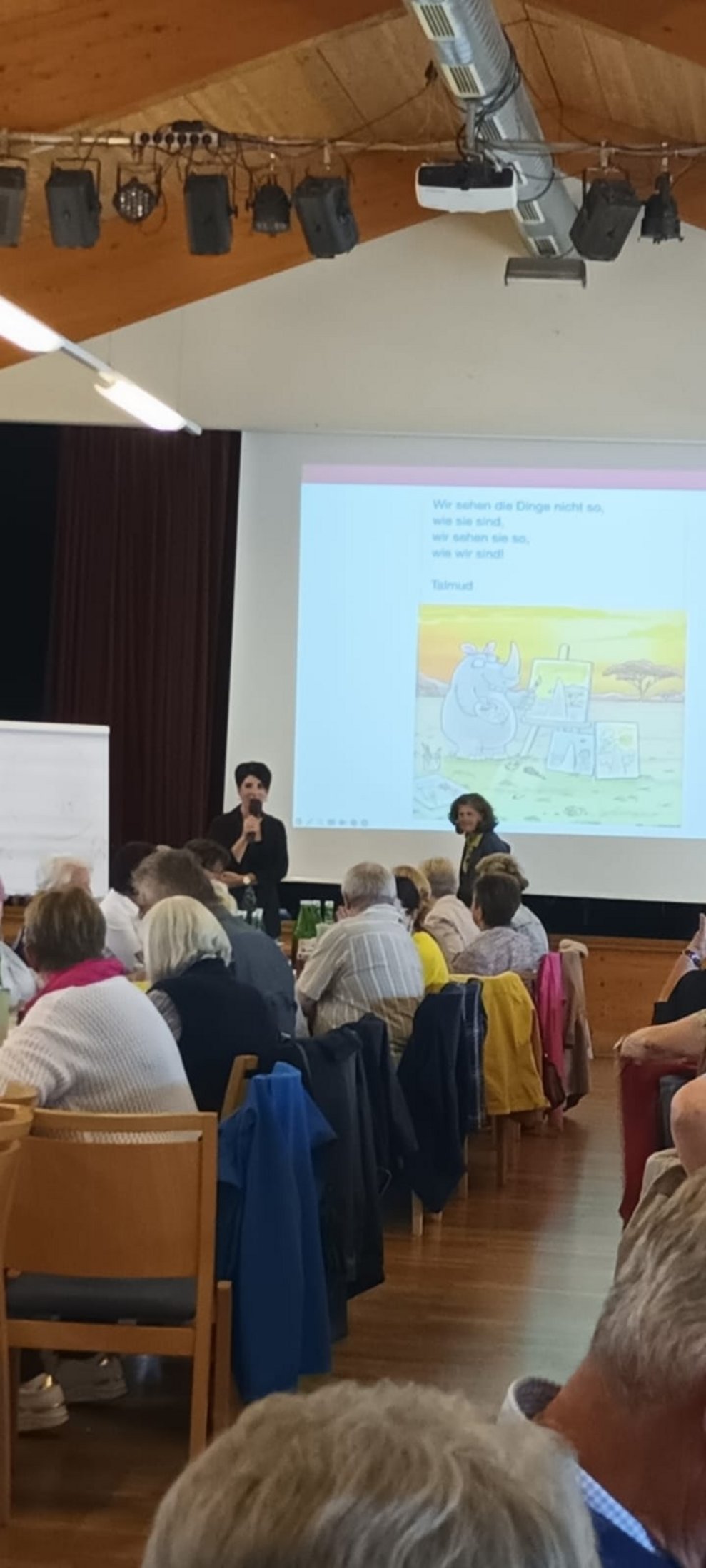 EA-Fortbildung: Ehrenamtlich Tätige sitzen in großen Saal beim Dia-Vortrag. Frau redet.