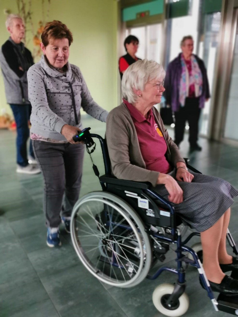 ehrenamtliche Mitarbeiterin schiebt Frau mit Rollstuhl
